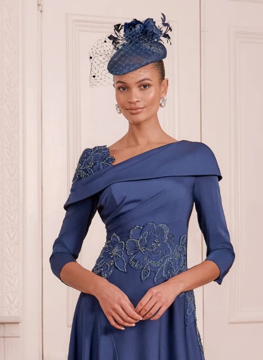 66797 Navy 2 - Sofi Designs Bridal Woman in a cobalt blue off-the-shoulder gown with floral beading and a matching fascinator hat.