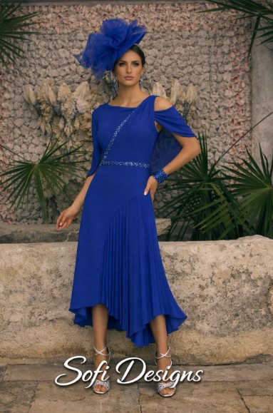 992785 Royal Blue 1 - Sofi Designs Bridal Model in a cobalt blue dress with off-shoulder sleeves, a pleated asymmetric hem, and matching accessories, wearing a large blue feather fascinator outdoors.