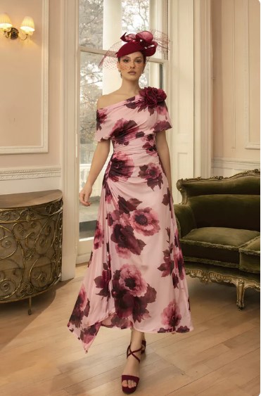 992827 Blush Wine print - Sofi Designs Bridal Woman in a pink floral off-shoulder gown with large burgundy roses, wearing a matching burgundy fascinator, standing in an elegant room with a green sofa.
