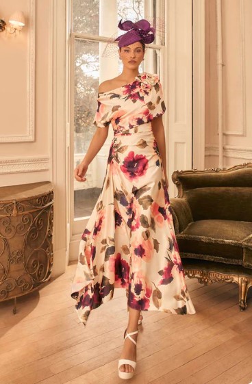 992827 Champagne print - Sofi Designs Bridal Elegant woman in a flowing off-shoulder floral gown with pink and purple blooms, white heels, and a purple headwrap in a classic room setting.