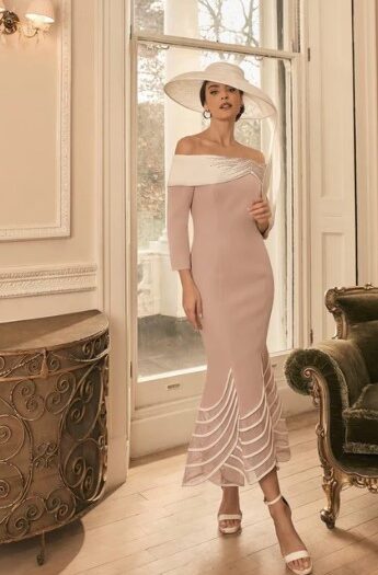 Woman in a pale pink off-shoulder midi dress and a white wide-brim hat, standing by a window in an ornate, sunlit room.