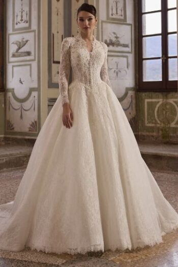 Bride wearing an ivory lace wedding gown with long sleeves and a full, voluminous skirt, standing in a historic, ornate room.