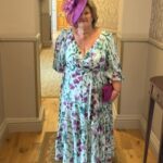 1 - Sofi Designs Bridal Woman in a blue floral dress with a large purple hat and pink clutch, standing in a hallway of a hotel or venue.