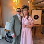 1 - Sofi Designs Bridal Couple posing indoors at a formal event: man in a light green suit and sunglasses, woman in a pale pink dress with a black fascinator headpiece.